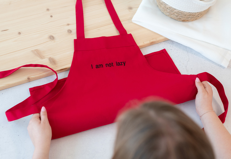 Rött barnförkläde med texten "I am not lazy" i svart på framsidan.